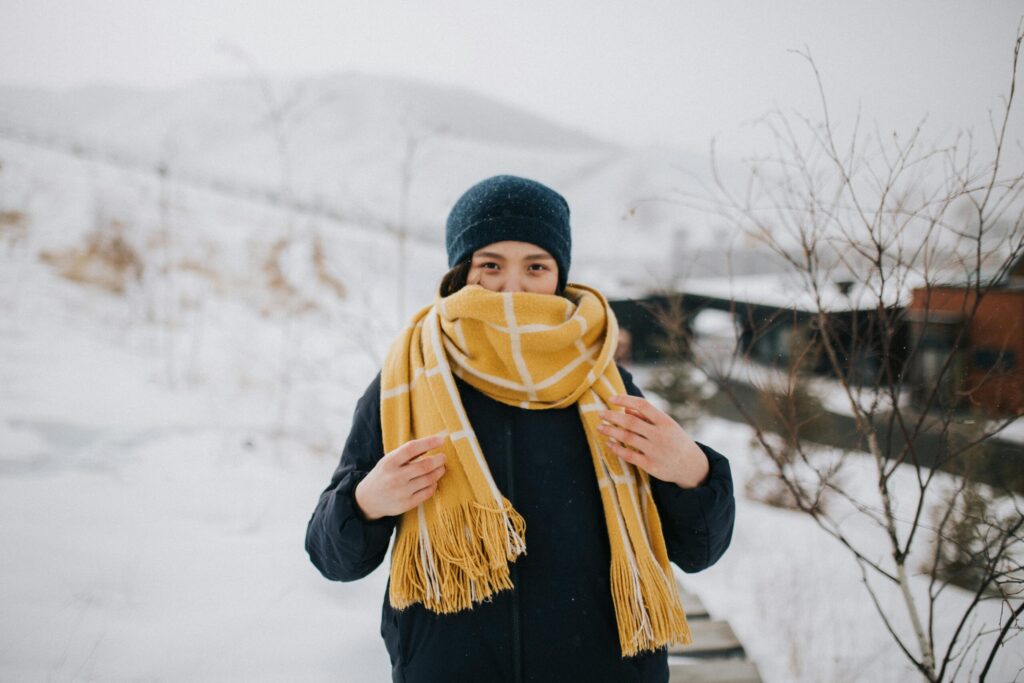 A woman wrapped in a warm scarf stands outdoors in a snowy Mongolian winter scene, showcasing cold weather fashion.