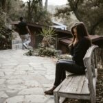 A woman sits pensively on a bench outside after a breakup, while a man walks away.