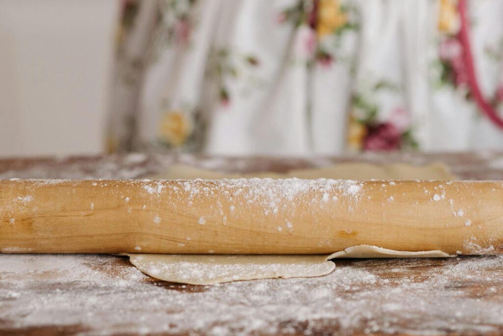 A wooden rolling pin rolling out dough on a flour-dusted surface, perfect for baking themes.