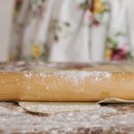 A wooden rolling pin rolling out dough on a flour-dusted surface, perfect for baking themes.