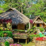 Rustic huts nestled in a lush garden with colorful flowers creating a serene atmosphere.