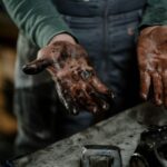 Close-up of a mechanic's dirty hands in a garage workspace with grease and spare parts.