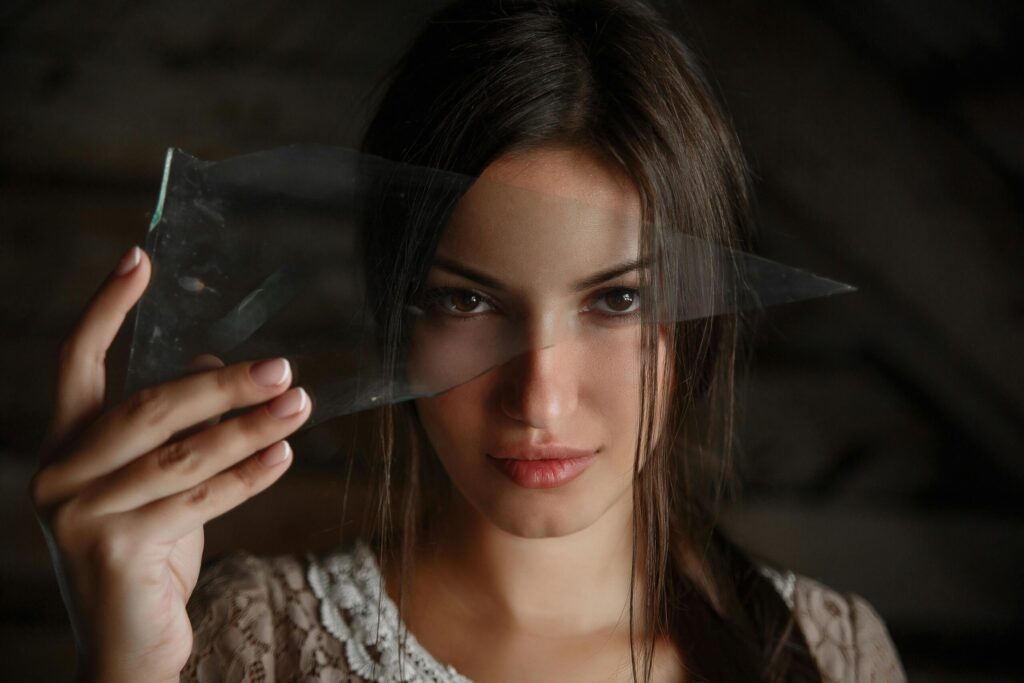 A dramatic portrait of a woman holding a piece of shattered glass, creating an abstract visual effect.