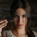 A dramatic portrait of a woman holding a piece of shattered glass, creating an abstract visual effect.