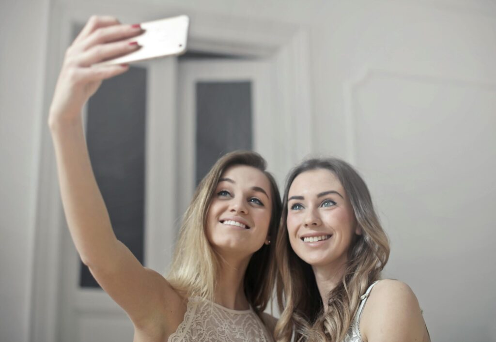 Two smiling women capturing a joyful selfie indoors, showcasing friendship and happiness.