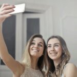 Two smiling women capturing a joyful selfie indoors, showcasing friendship and happiness.
