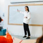 Smiling teacher instructing students in a classroom setting using a whiteboard.