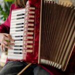 Musician's hands playing an accordion indoors with focus on keys and buttons.