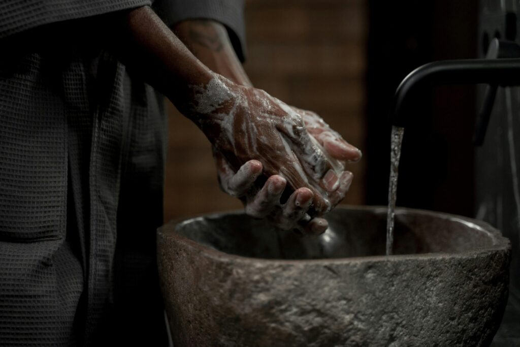 Man washing hands with soap in stone basin for hygiene and cleanliness.