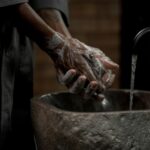 Man washing hands with soap in stone basin for hygiene and cleanliness.