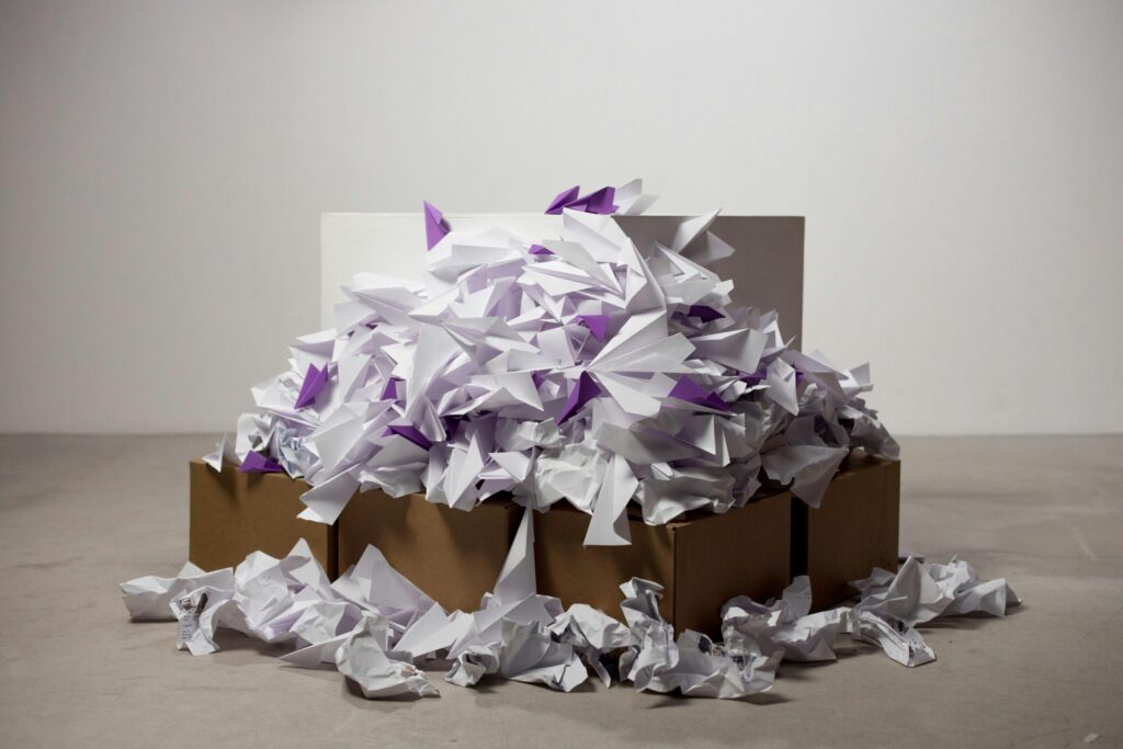 A large pile of origami paper planes overflowing from cardboard boxes on a plain background.