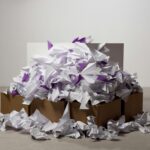A large pile of origami paper planes overflowing from cardboard boxes on a plain background.