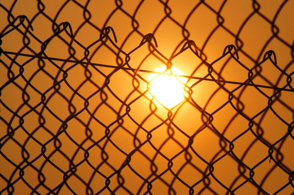 Dramatic shot of the sunset through a chain-link fence, creating a silhouette effect.