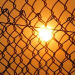 Dramatic shot of the sunset through a chain-link fence, creating a silhouette effect.