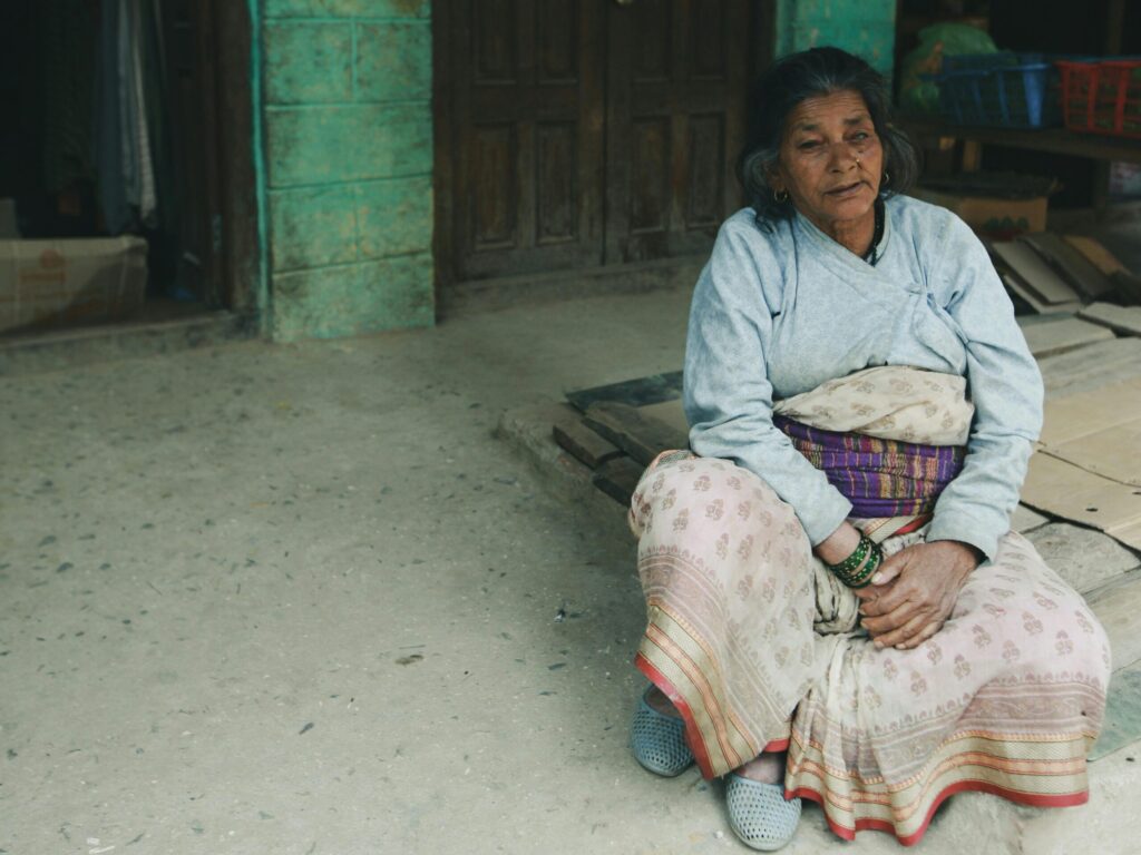 An elderly woman in traditional clothing sits outdoors, exuding cultural richness and simplicity.