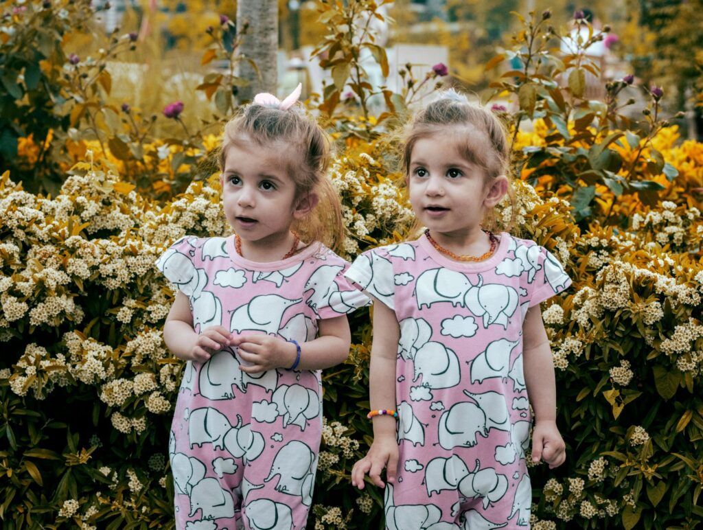 Charming twin girls in elephant print dresses amidst autumn blooms in Istanbul.