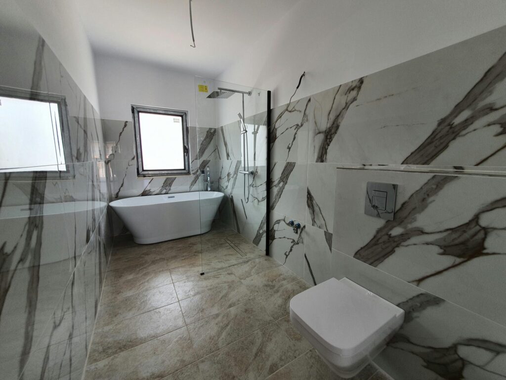 Bright contemporary bathroom with marble tiling, freestanding tub, and natural light in Iași, Romania.