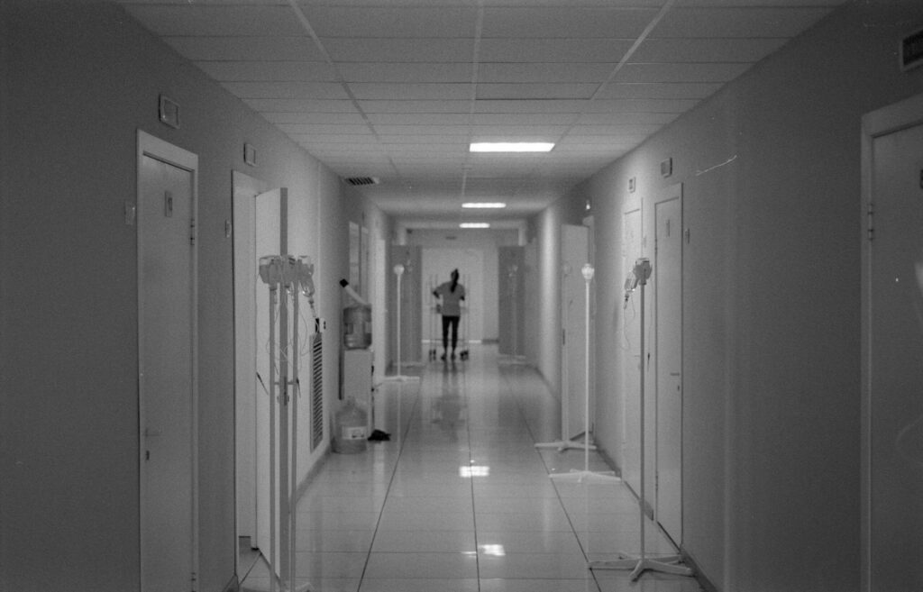 Monochrome image of a hospital hallway with a nurse in the background, highlighting healthcare environment.