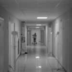 Monochrome image of a hospital hallway with a nurse in the background, highlighting healthcare environment.