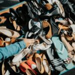 A variety of footwear displayed at an outdoor market stall with a hand selecting a shoe.