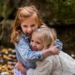 Two joyful sisters hugging outdoors in autumn, surrounded by fallen leaves.