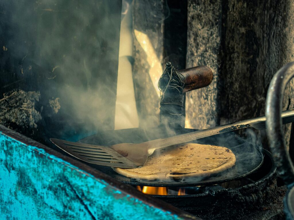 A rustic scene of flatbread cooking on an open flame with a spatula.