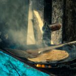 A rustic scene of flatbread cooking on an open flame with a spatula.
