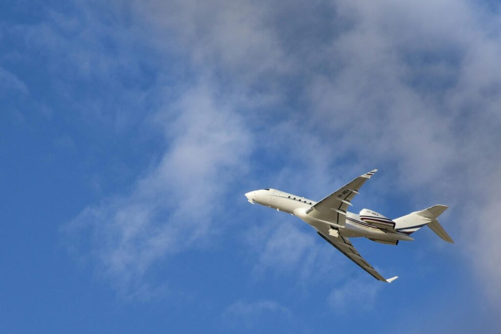 Commercial jet airplane flying high with a clear blue sky and clouds in the backdrop.