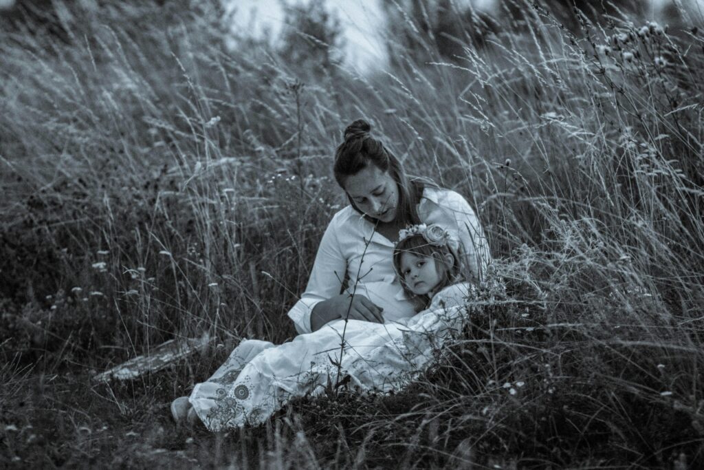 A calming scene of a mother and daughter sitting amidst tall grass, creating a peaceful bond.