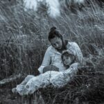 A calming scene of a mother and daughter sitting amidst tall grass, creating a peaceful bond.