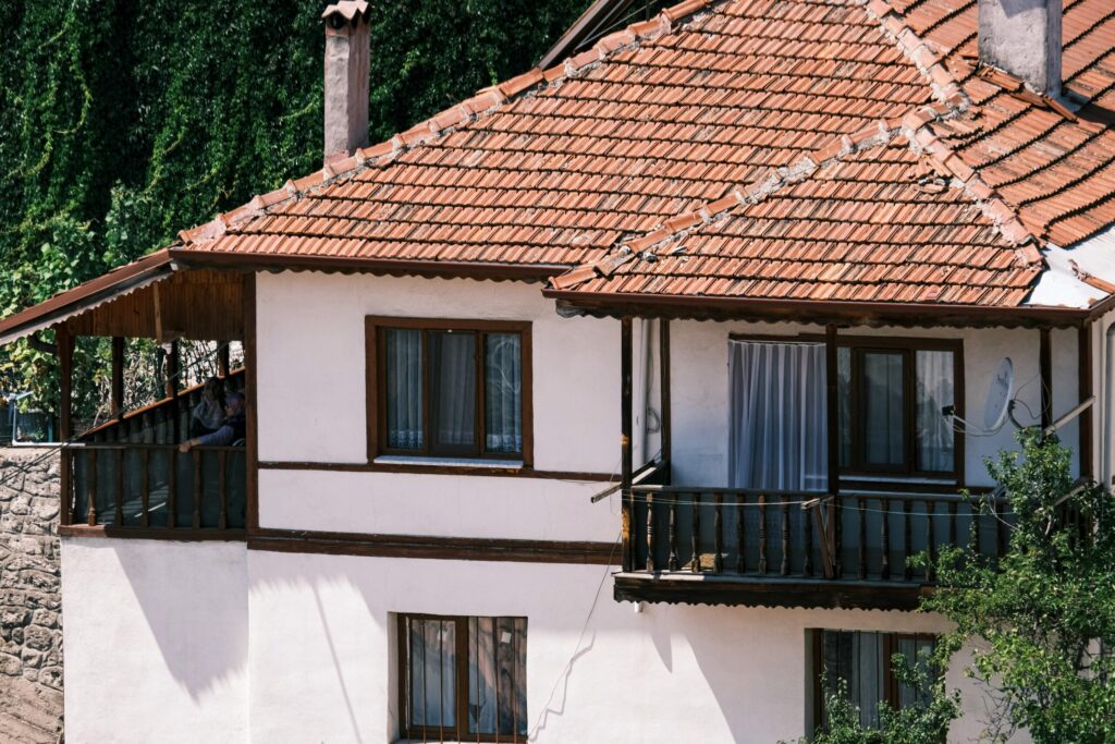 A traditional rustic house with a red tiled roof and wooden balcony in a sunny setting.