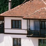 A traditional rustic house with a red tiled roof and wooden balcony in a sunny setting.