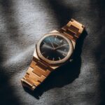 Close-up of a gold analog watch with a sleek design, artfully lit to highlight its elegance and style.