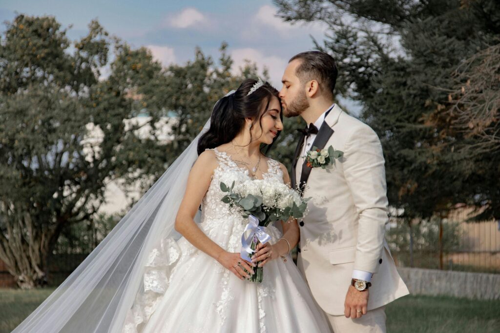A romantic outdoor portrait of a bride and groom sharing a tender moment on their wedding day.