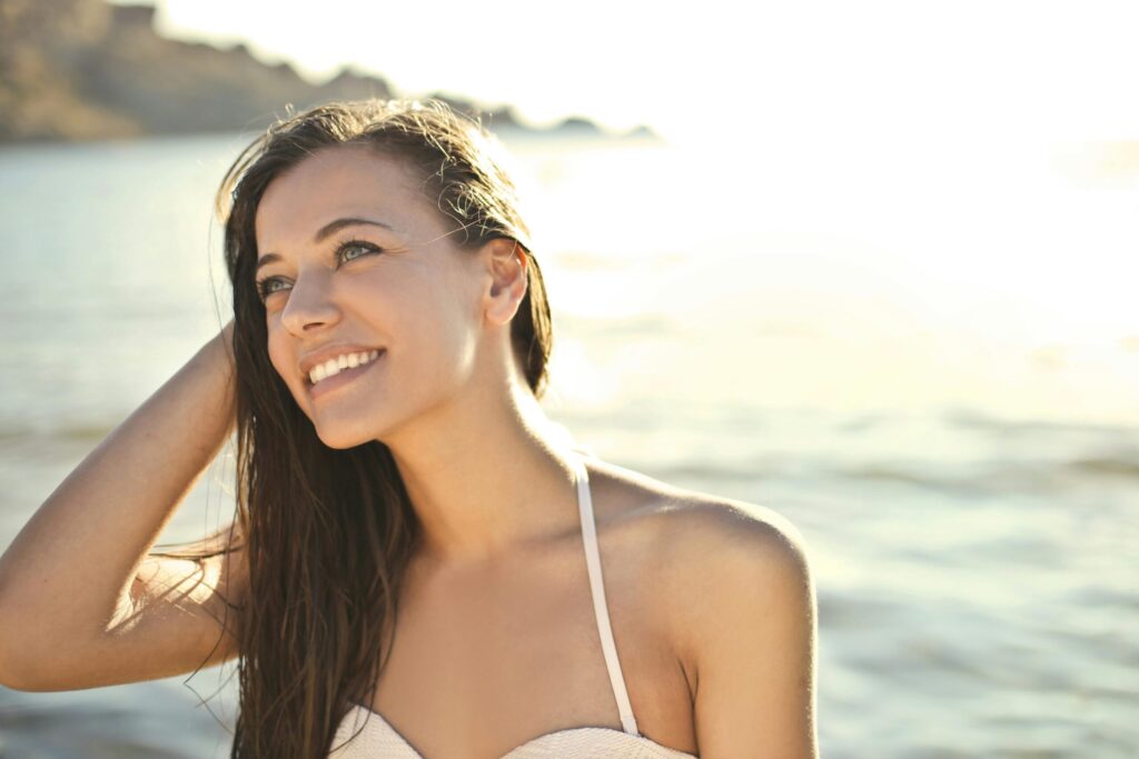 A woman enjoying a sunny day at the beach, smiling in her swimsuit.