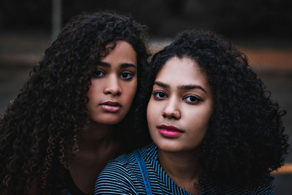 Close-up portrait of two women with curly hair in a serene outdoor setting.