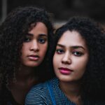 Close-up portrait of two women with curly hair in a serene outdoor setting.