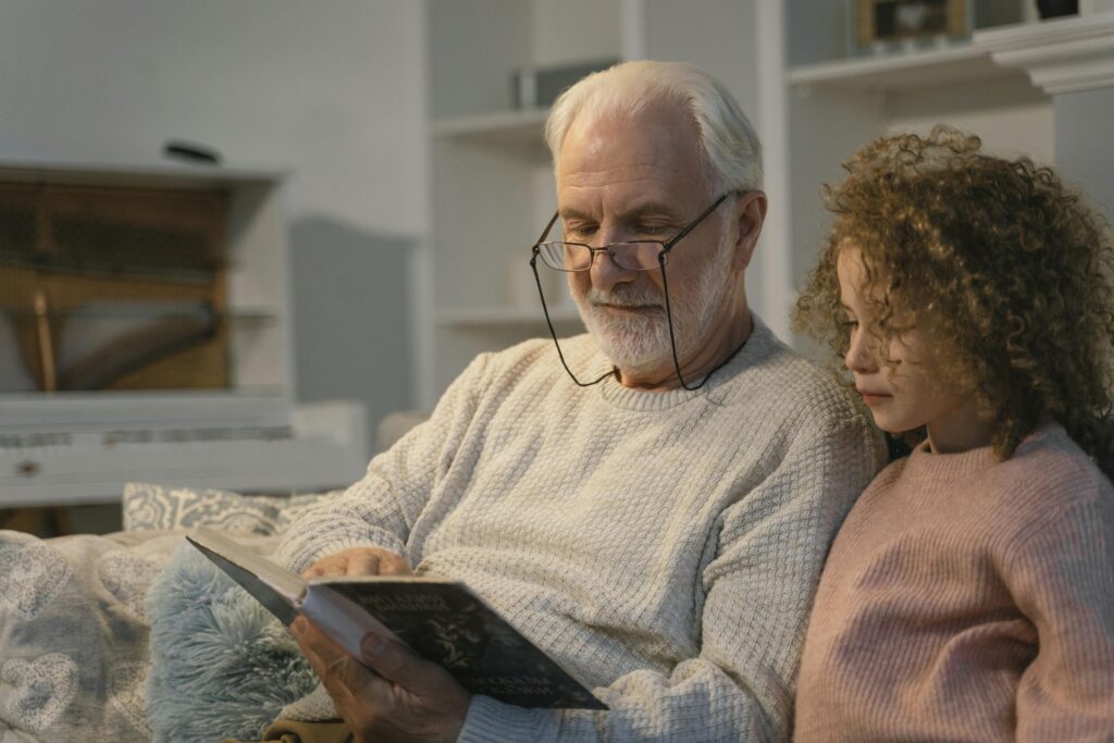 Elderly man and girl reading a book together at home, sharing a cherished moment.