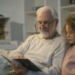 Elderly man and girl reading a book together at home, sharing a cherished moment.