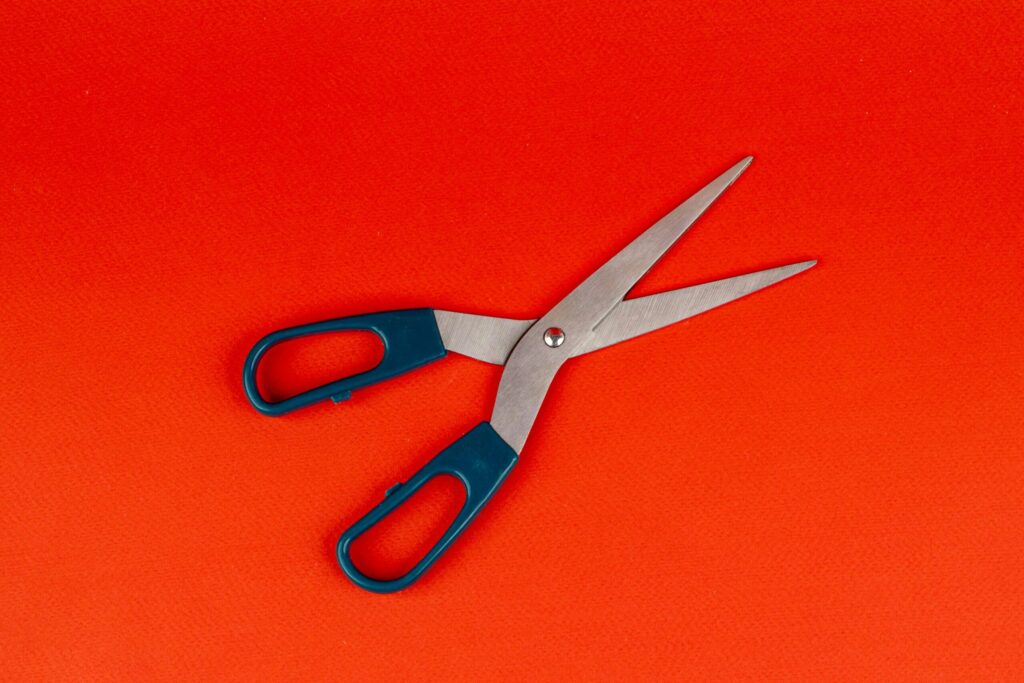A pair of scissors with blue handles lies open on a bright orange background.