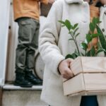 A couple carrying plants in a wooden box while moving into a new home.