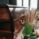 A beautiful funeral display featuring a wooden coffin with flowers and candles indoors.