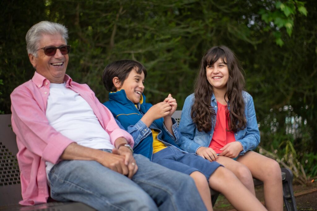 Grandfather with grandchildren laughing together on a park bench in Portugal.