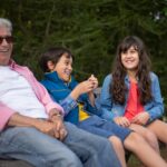 Grandfather with grandchildren laughing together on a park bench in Portugal.