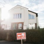 Bright suburban house exterior with a for sale sign in the foreground.