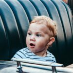 Cute child with surprised expression sitting in a car seat wearing a striped shirt.