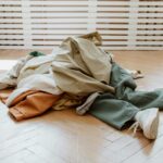 Pile of casual clothes on a wooden floor in a minimalistic room.