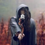 A hooded figure holds a staff in a misty, autumn forest setting, evoking mystery and fantasy.