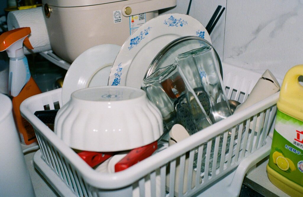Clean kitchenware including plates and glasses drying in a dish rack with cleaning supplies nearby.