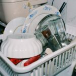 Clean kitchenware including plates and glasses drying in a dish rack with cleaning supplies nearby.